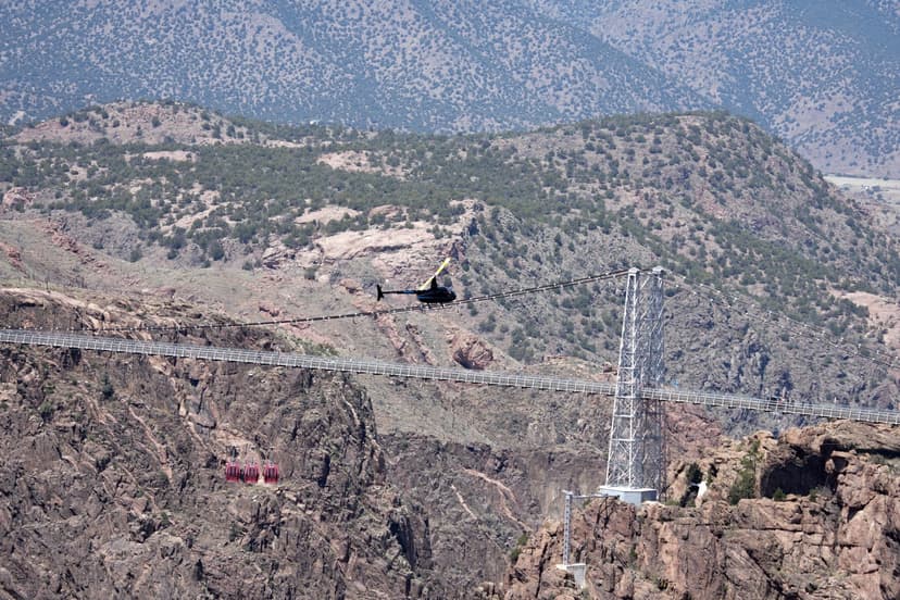 Robinson R44 helicopter approaching Royal Gorge Bridge suspension tower with gondola visible below
