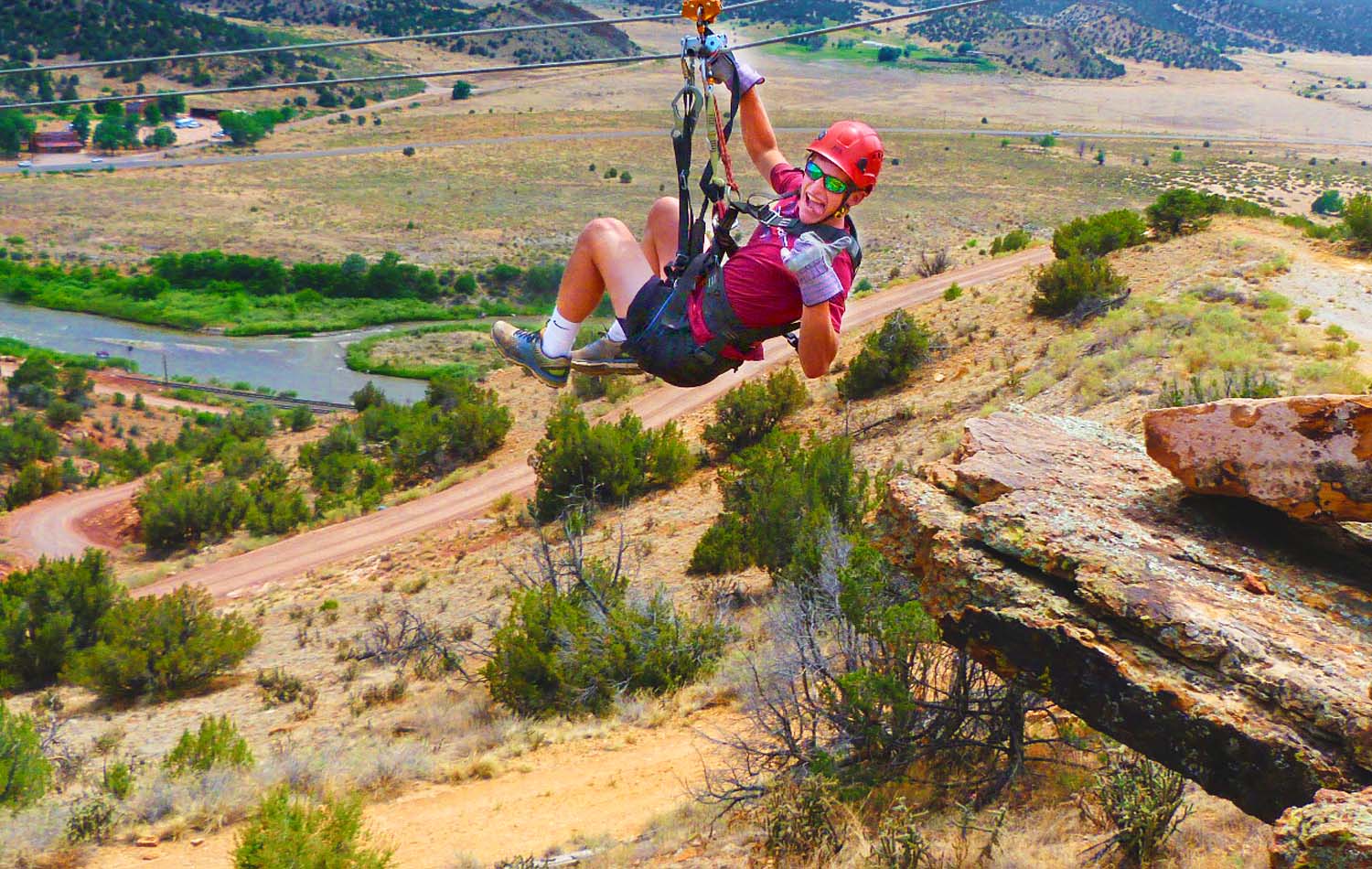 Zipline riders soaring over the Arkansas River valley with Royal Gorge canyon and Colorado mountains in the background