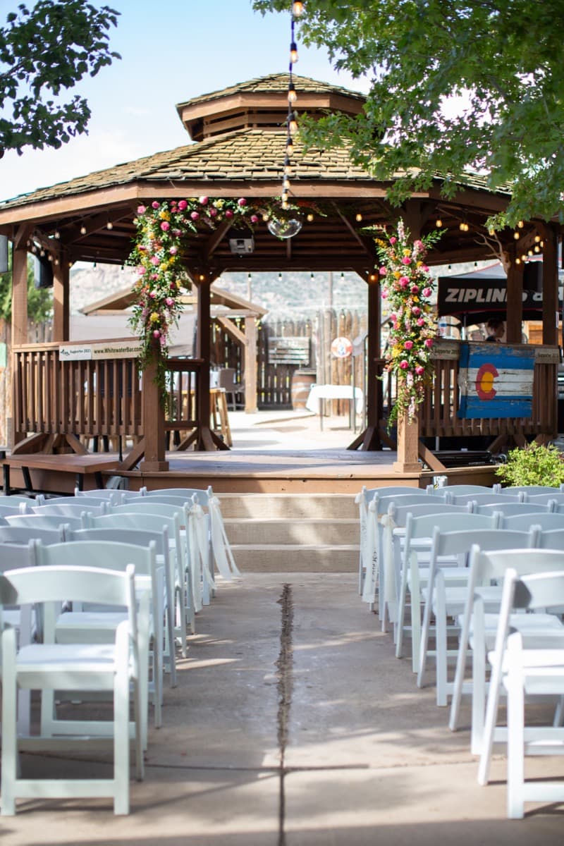 Wedding ceremony setup at WWBG gazebo with floral arch, white chairs, and string lights under Colorado sky