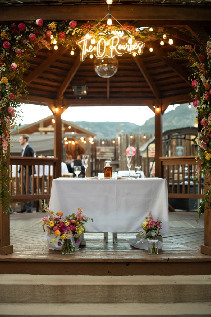 Neon sign illuminating sweetheart table with wildflower centerpieces at WWBG wedding reception